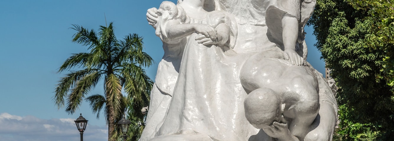 Una estatua de mármol blanco de una mujer y un niño en un parque.