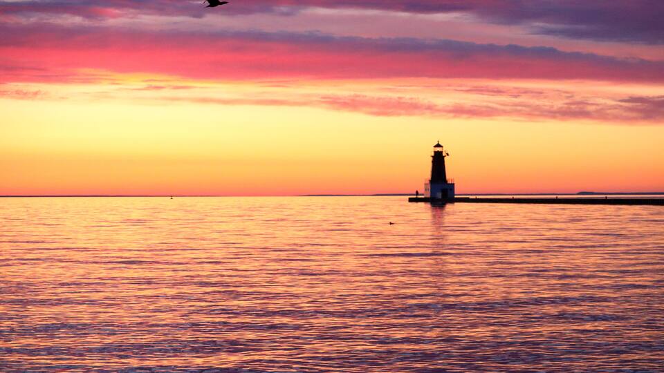 A lighthouse at sunset with a bird flying in the sky.
