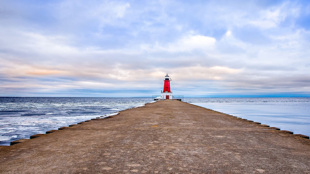 Ein Leuchtturm auf einem Steg, der sich ins Meer erstreckt, unter einem bewölkten Himmel.