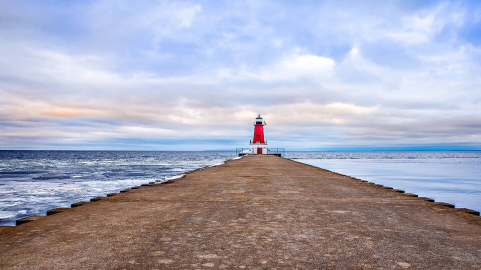 A lighthouse on a pier extending into the sea under a cloudy sky.