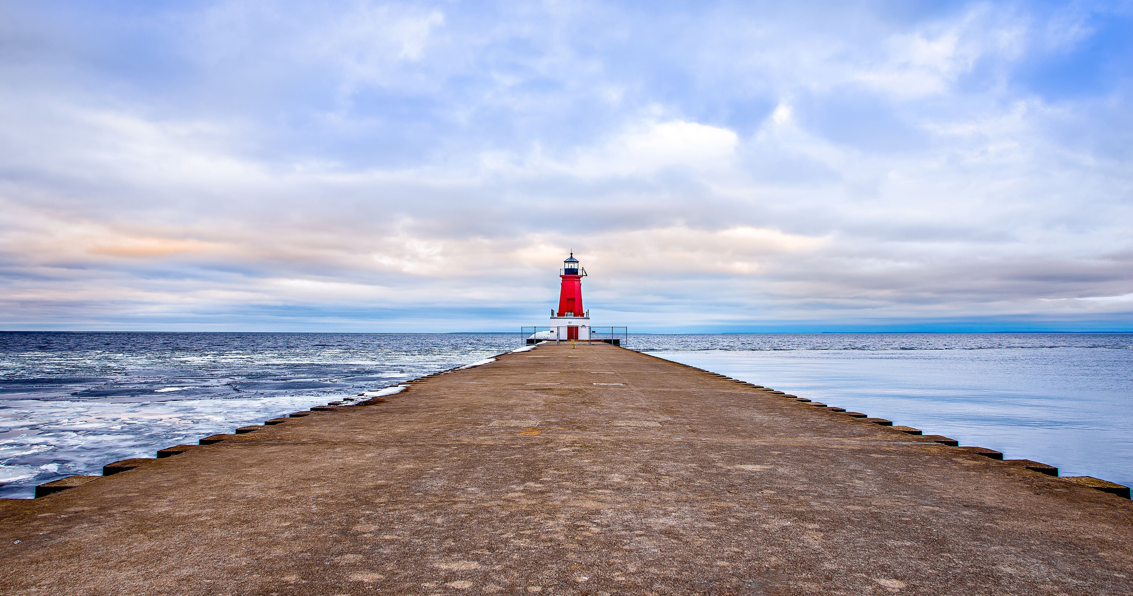 A lighthouse on a pier extending into the sea under a cloudy sky.