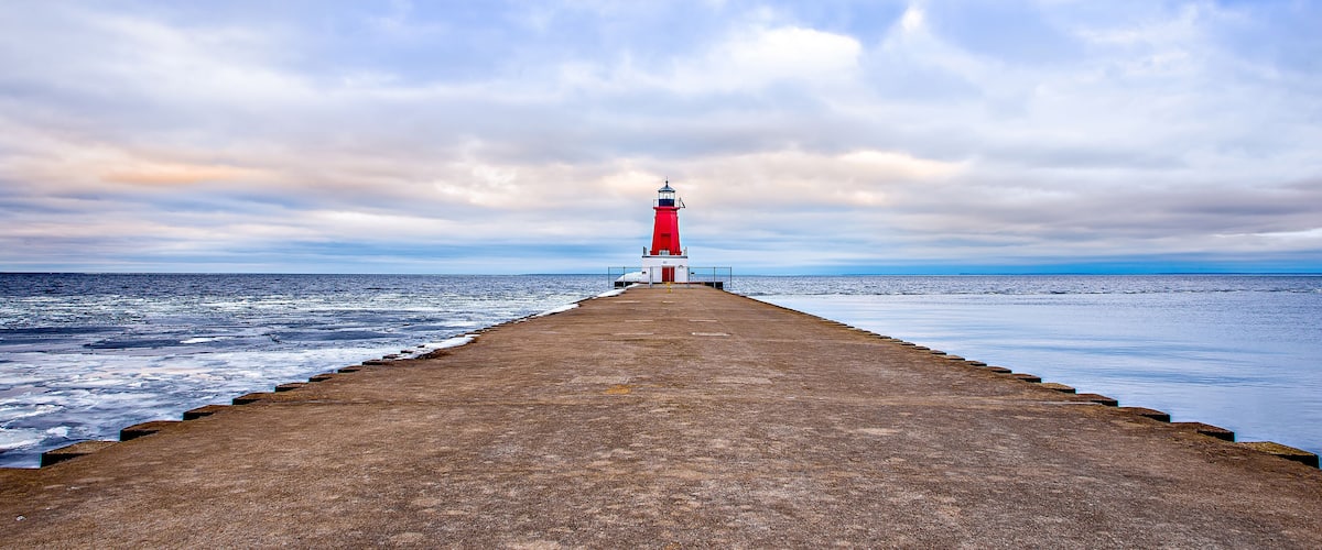 A lighthouse on a pier extending into the sea under a cloudy sky.