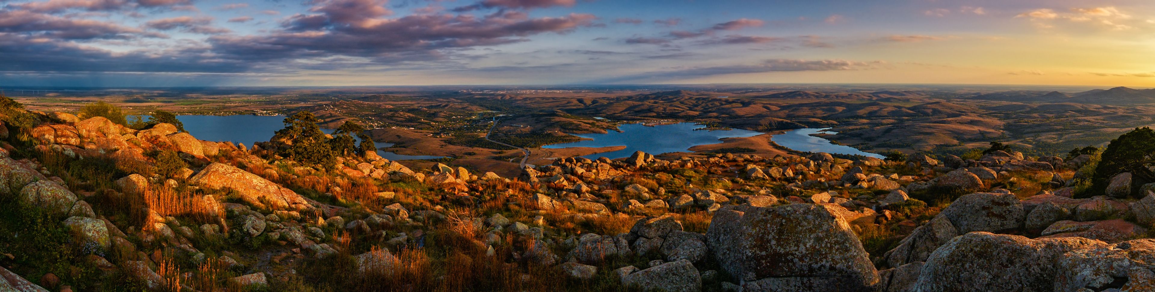 Paisagem montanhosa com terreno rochoso, um rio e árvores dispersas.
