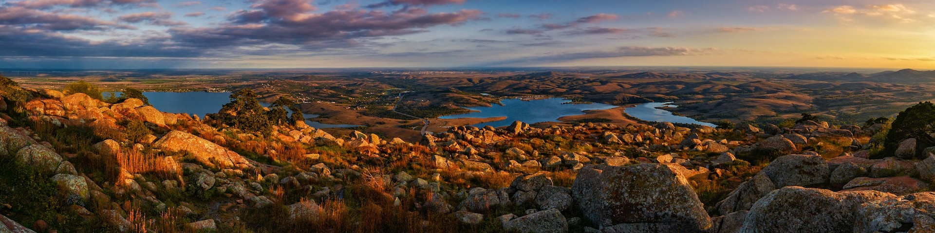 Paisagem montanhosa com terreno rochoso, um rio e árvores dispersas.