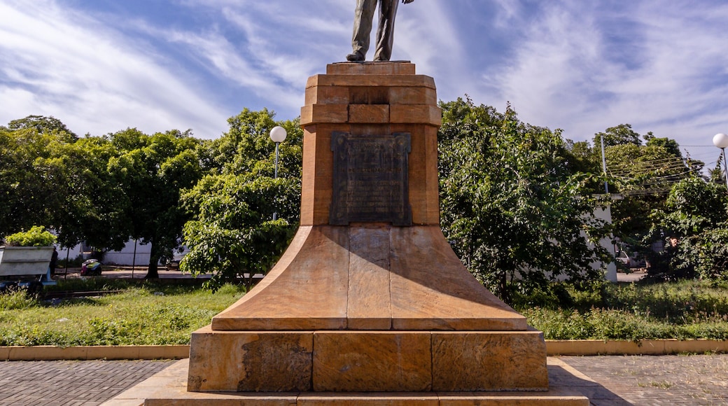 A statue on a pedestal in a park with trees and a clear sky.
