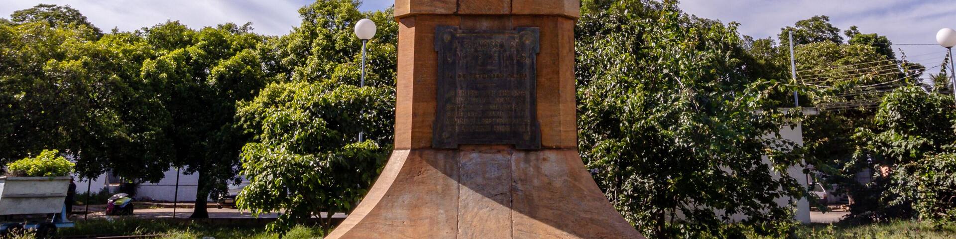 A statue on a pedestal in a park with trees and a clear sky.