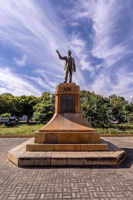 Una estatua sobre un pedestal en un parque con árboles y cielo despejado.