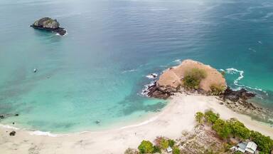 A top-down drone shot of an idyllic Koka Beach. Hidden gem of Flores, Indonesia. Headland going straight into the open sea. Beauty in the nature. Calm waves washing the cliff's slopes. Serenity.