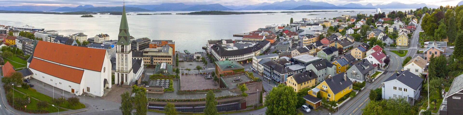 A coastal town with a prominent church, a roundabout, and a view of the sea and mountains in the background.