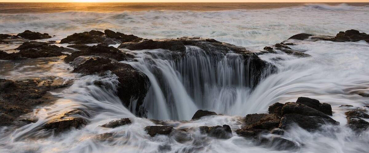 Thor's Well on the Oregon coast appears to be the end of the earth. Also known as the drainpipe of the Pacific, the well is actually a hole in the rock that only appears to drain water from the ocean. In reality the huge hole is likely only around 10 meters deep. Even if the well is not quite as magic as it seems, it still manages to produce amazing sights, though not for the faint of heart!.
The site is most spectacular at high tide when the water washes violently over the rocks and funnels into the hole. I arrived here just before sunset and as I made my way down to the spot I saw small group of photographers standing on a rock right in front of the hole with their tripods already setup and taking photos. I managed to squeeze myself between a couple of photographers and began shooting however it wasn't long before the waves got higher and eventually swept up onto the rock we were all standing on, soaking our feet. We would have easily been swept away by the torrent had it not been for the rock we were all standing on. The sky was stormy and as the sun set over the horizon the colour in the sky turned a beautiful orange glow , perfect.