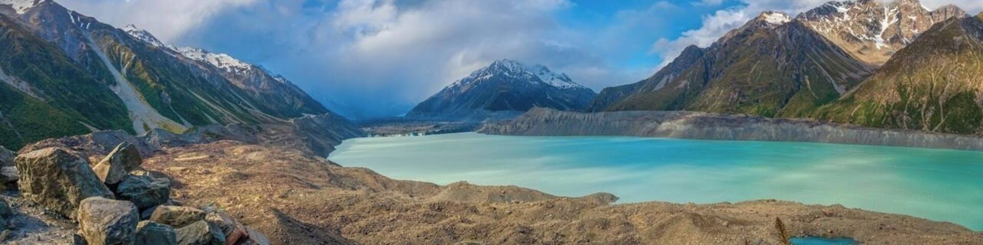 Un paisaje montañoso con un lago turquesa rodeado de terreno rocoso y cumbres nevadas.