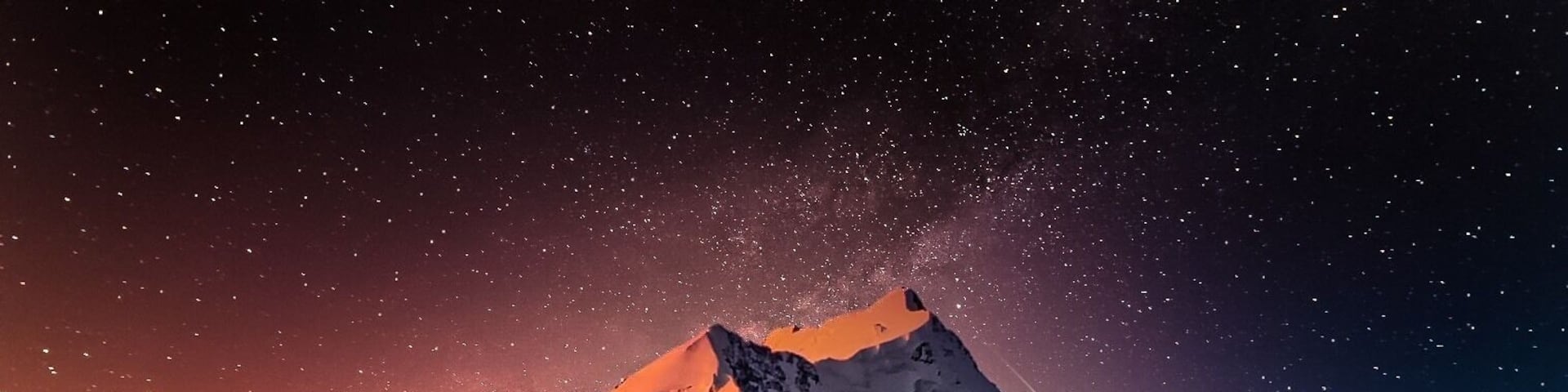 A snow-covered mountain peak under a starry night sky.
