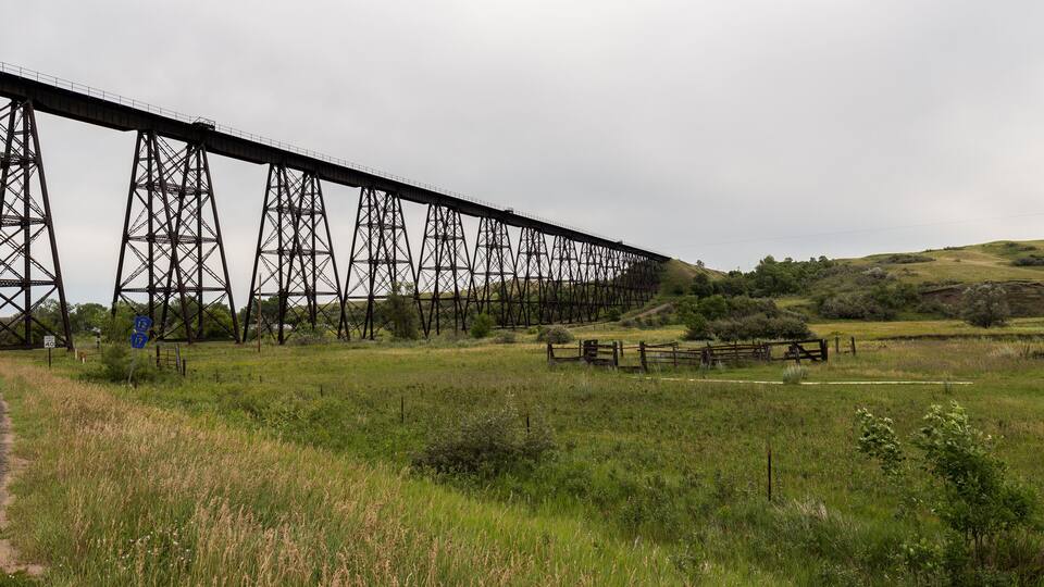 A railway bridge over a grassy field with a fence and a road sign.