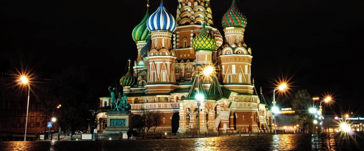 The illuminated Saint Basil's Cathedral with colorful domes and a statue in front.