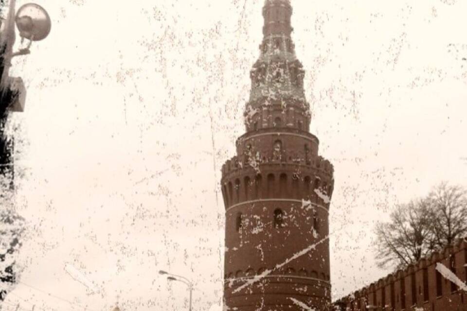 Ein historischer Turm mit einer spitz zulaufenden Turmspitze, umgeben von einer befestigten Mauer und einem Kuppelgebäude im Hintergrund.