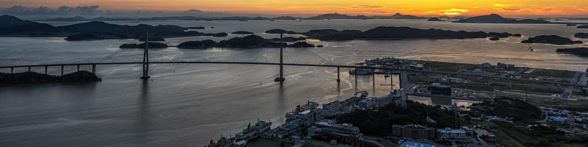 A sunset over a body of water with a bridge and distant islands.