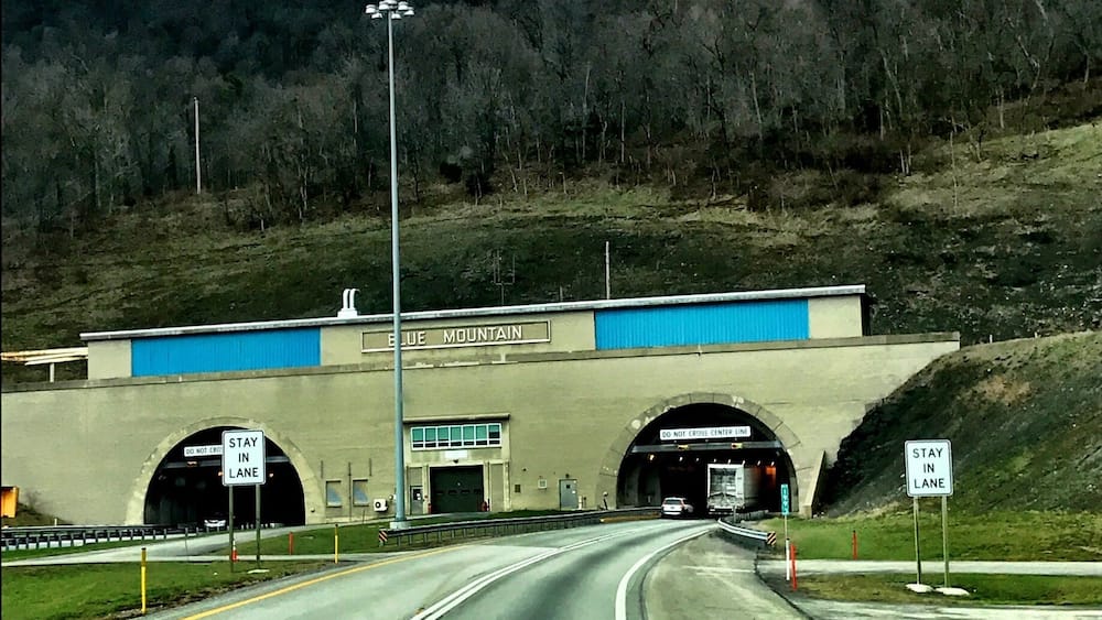 Tunnelportal einer Autobahn mit Schildern 'URCHEN VERBOTEN' und 'IN DER SPUR BLEIBEN'.