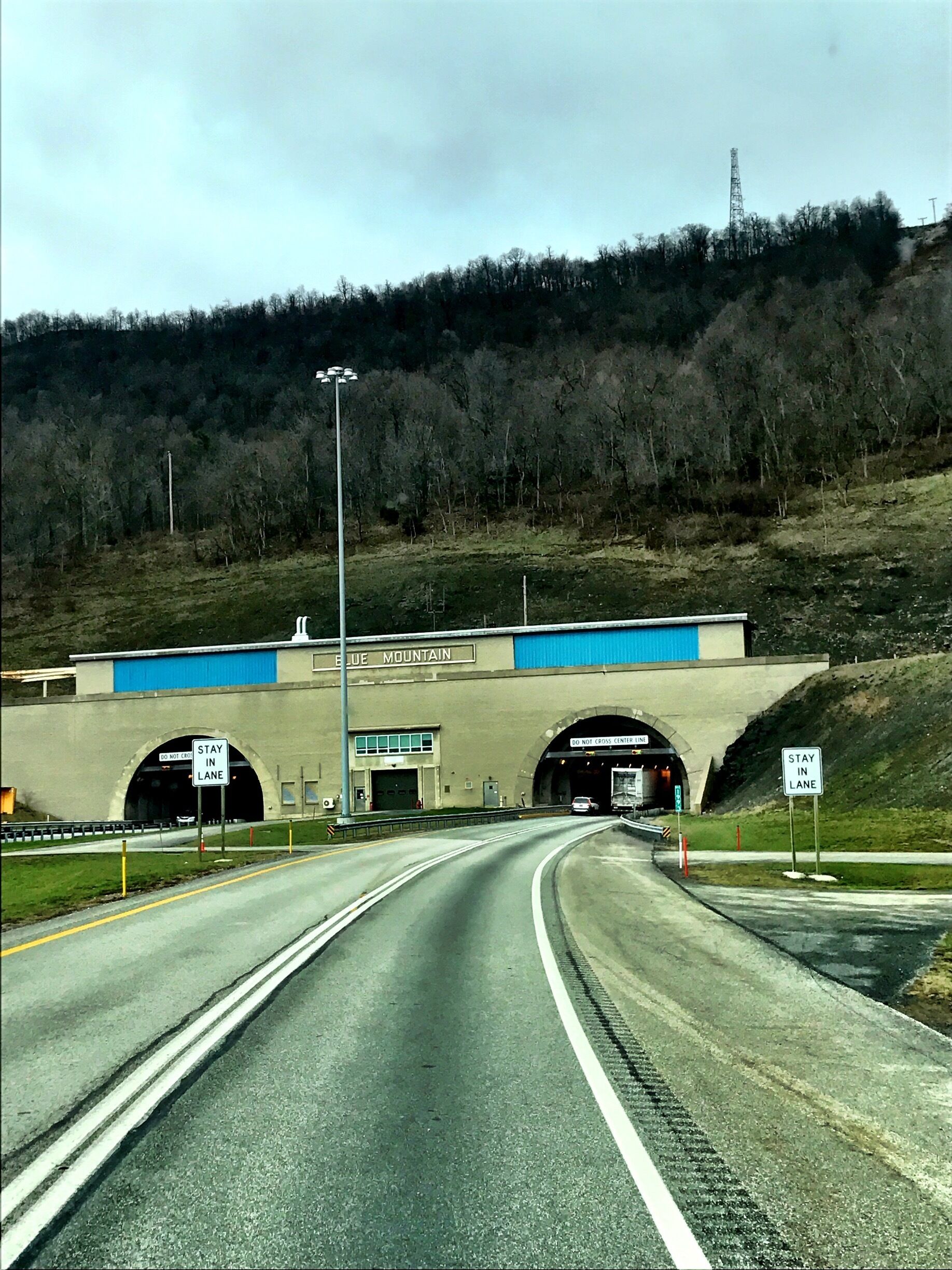 A highway tunnel entrance with 'DO NOT CROSS' signs and 'STAY IN LANE' signs.