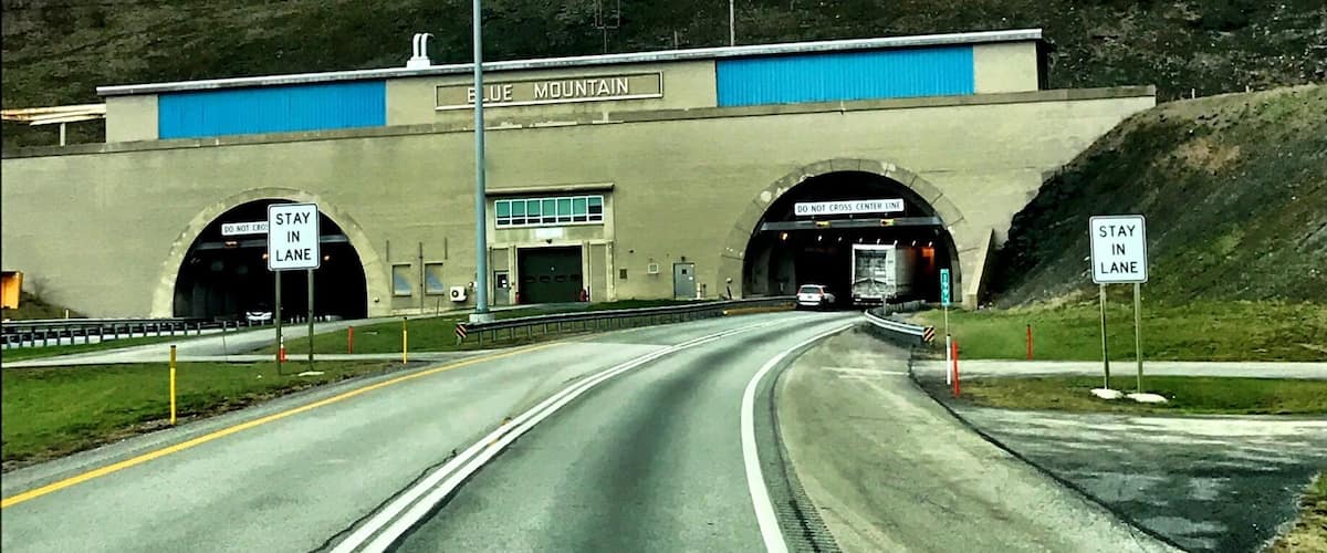 A highway tunnel entrance with 'DO NOT CROSS' signs and 'STAY IN LANE' signs.