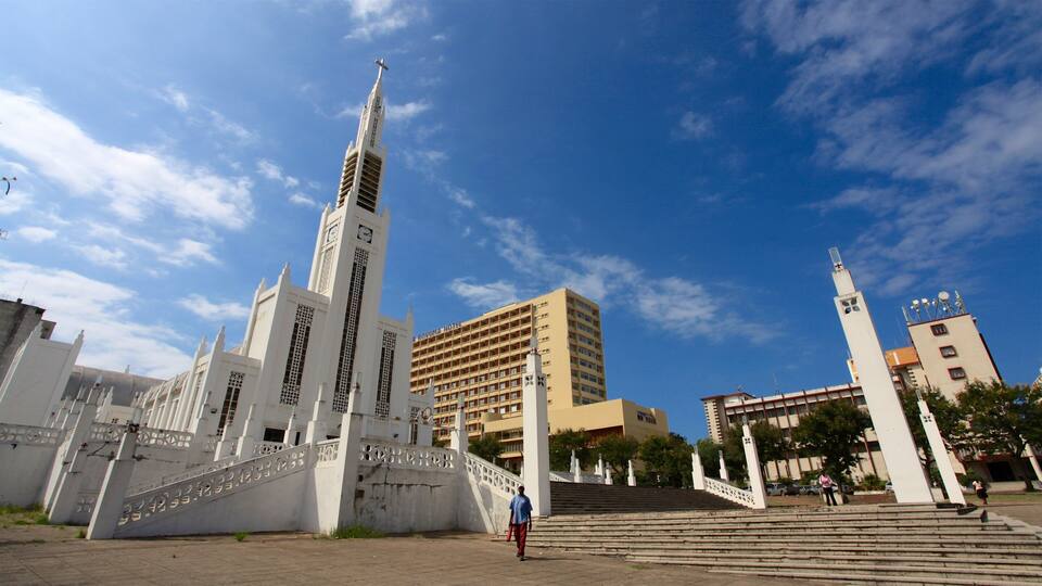 A large white building with a clock tower and a cross on top, surrounded by steps and a fence.