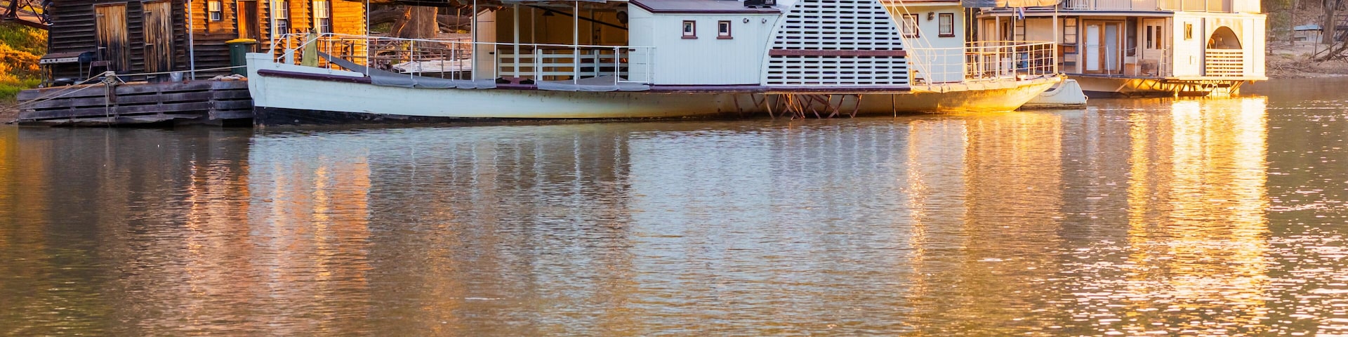 A houseboat docked on a calm river, surrounded by trees.
