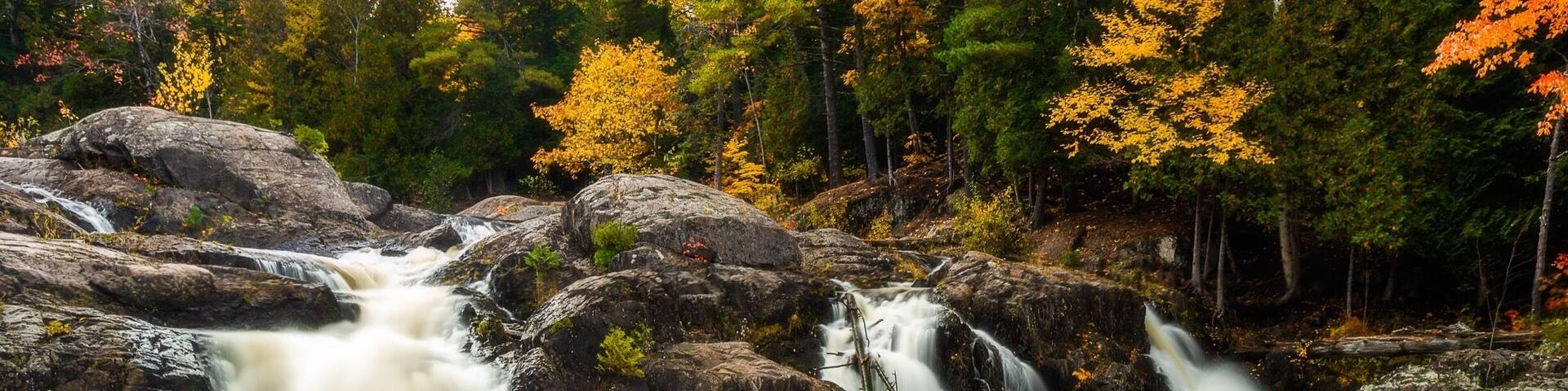 A waterfall cascading over rocks in a forested area with autumn-colored trees.