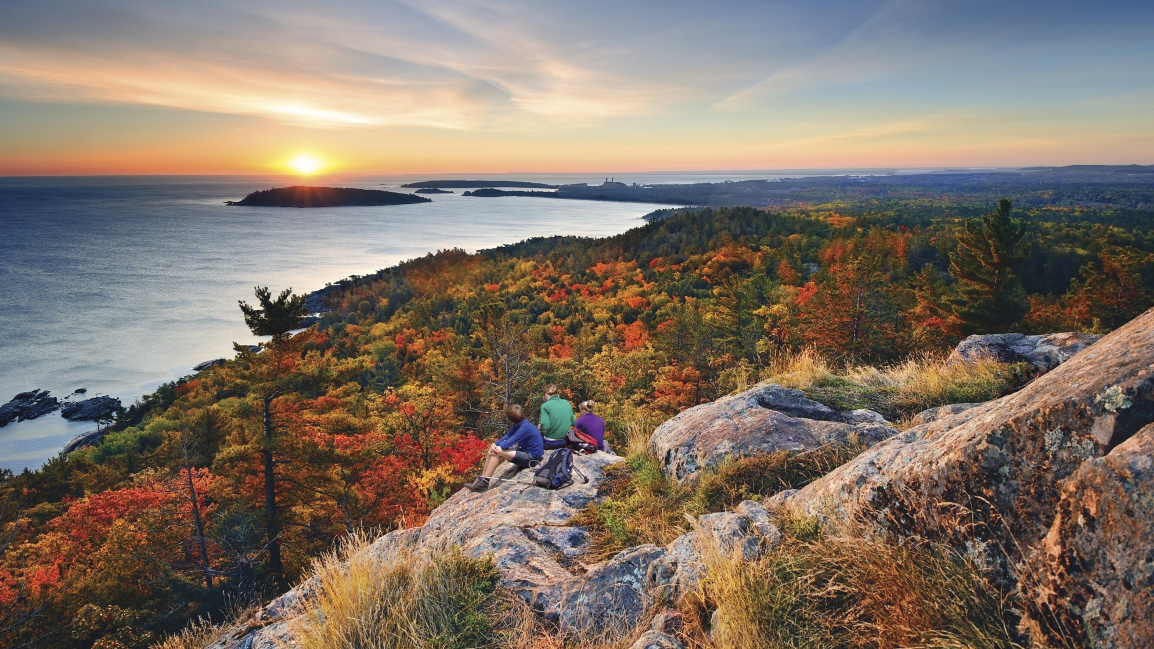 Marquette which includes general coastal views and a sunset as well as a small group of people