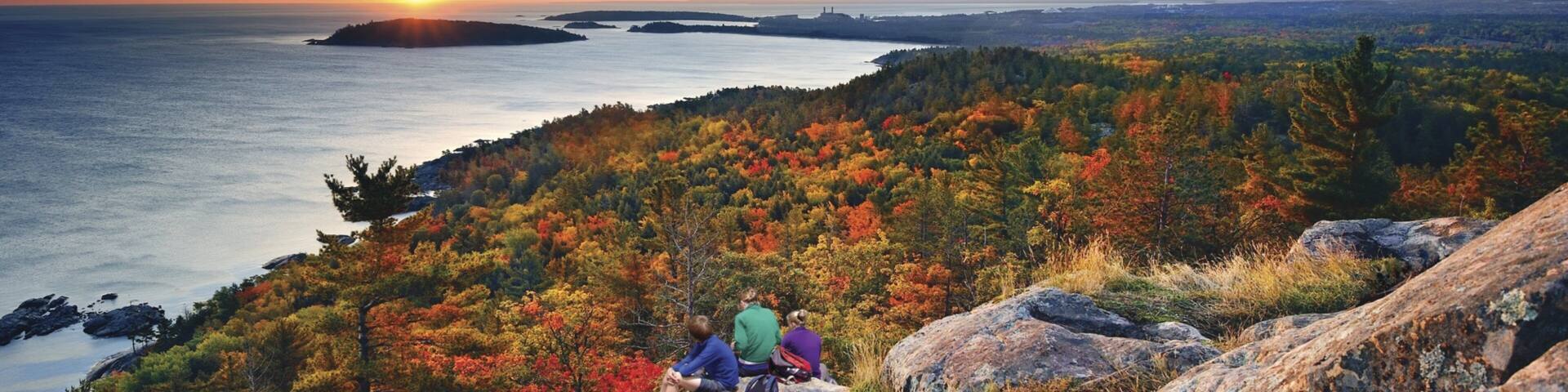 Marquette which includes general coastal views and a sunset as well as a small group of people