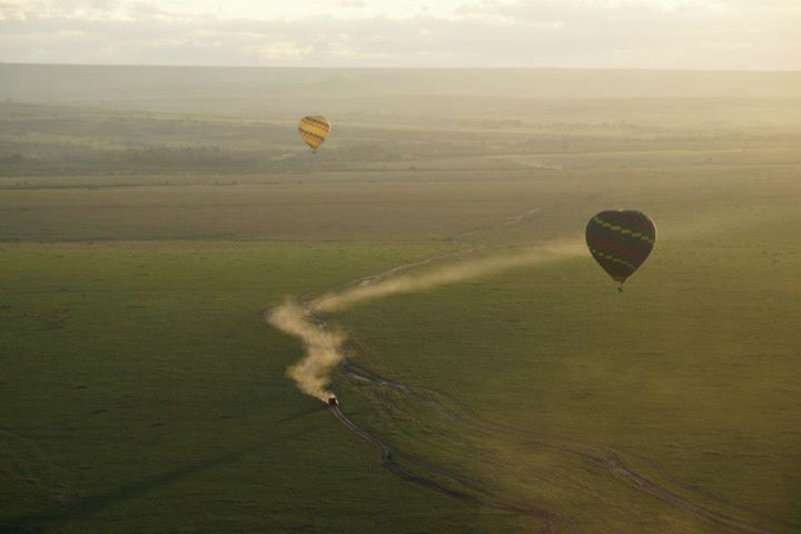Two hot air balloons flying over a vast, open landscape with a narrow path visible on the ground.