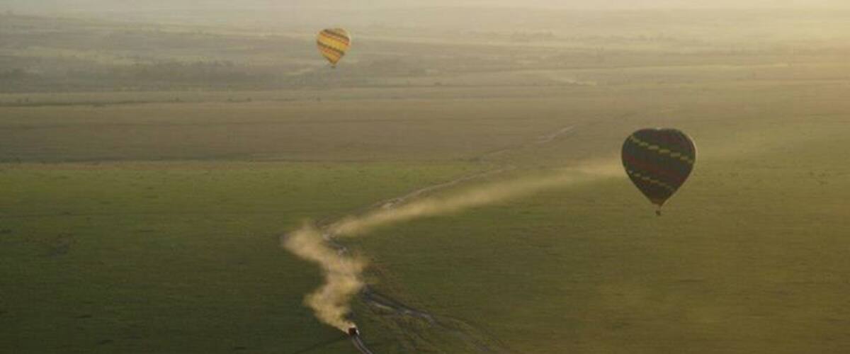 Two hot air balloons flying over a vast, open landscape with a narrow path visible on the ground.
