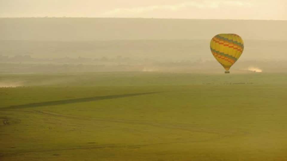 A hot air balloon over a green field with a hazy horizon.