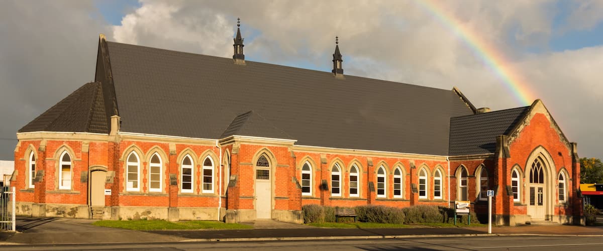 A red brick church with a large steeple and a rainbow in the sky.