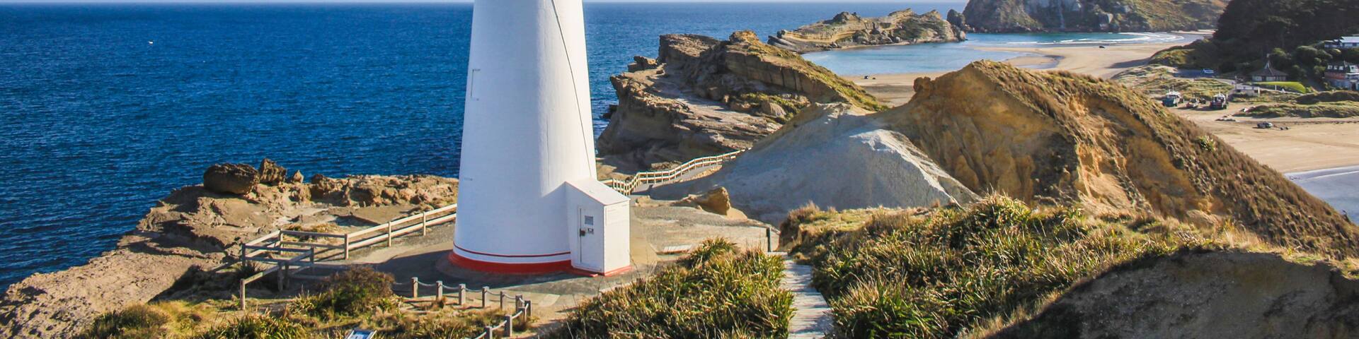 A white lighthouse with a green top, situated on a rocky coastline with clear blue waters.