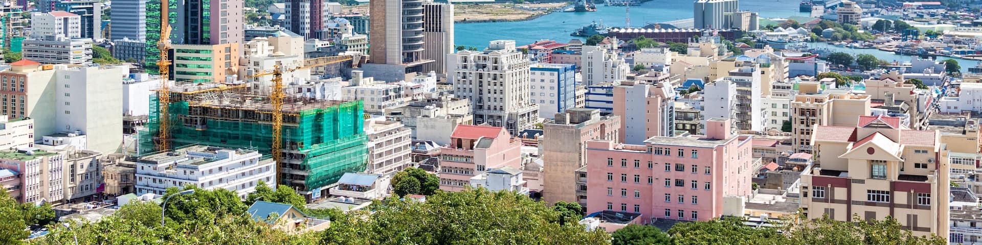 A coastal cityscape with a mix of modern and historic buildings, a prominent tower, and a view of the sea and a bridge in the distance.