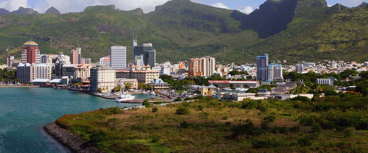 Un paisaje urbano costero con una imponente cadena montañosa al fondo.
