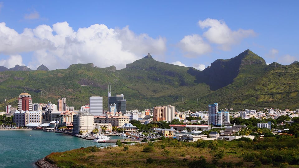 A coastal cityscape with a prominent mountain range in the background.