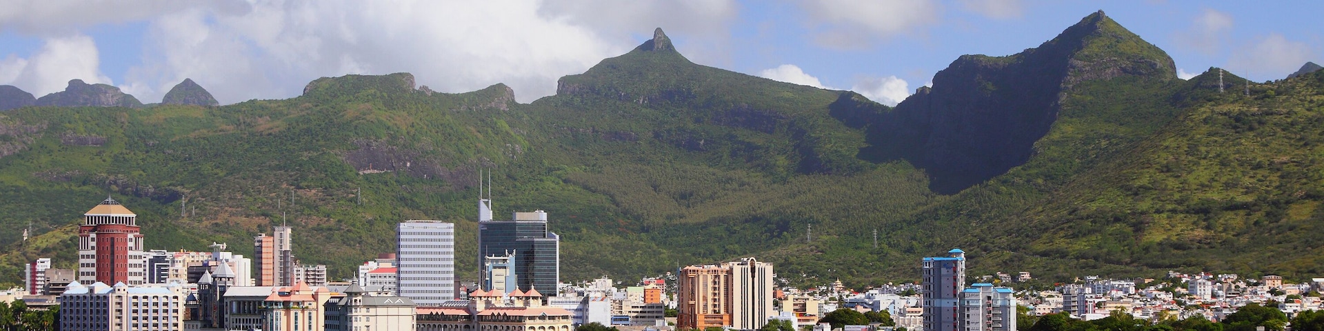 Un paisaje urbano costero con una imponente cadena montañosa al fondo.