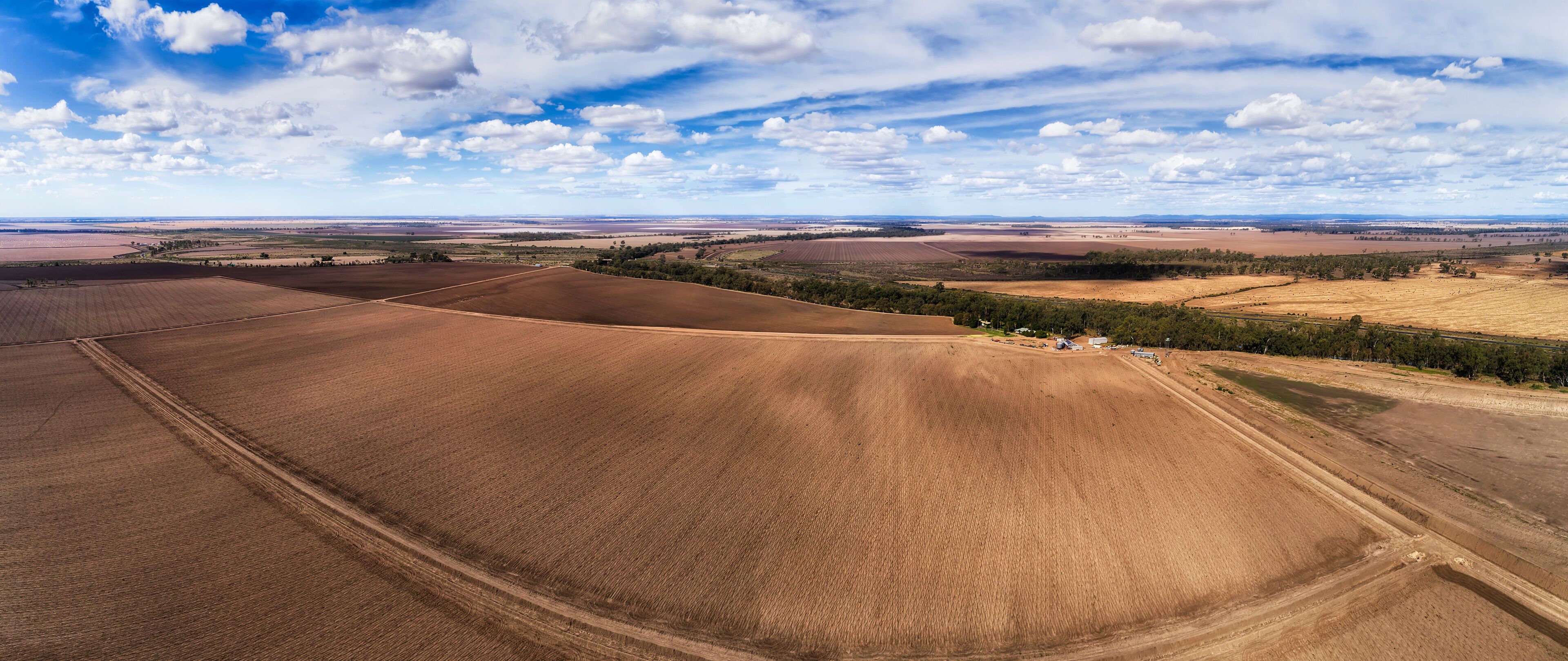 A vast agricultural landscape with expansive fields, a winding road, and scattered trees.