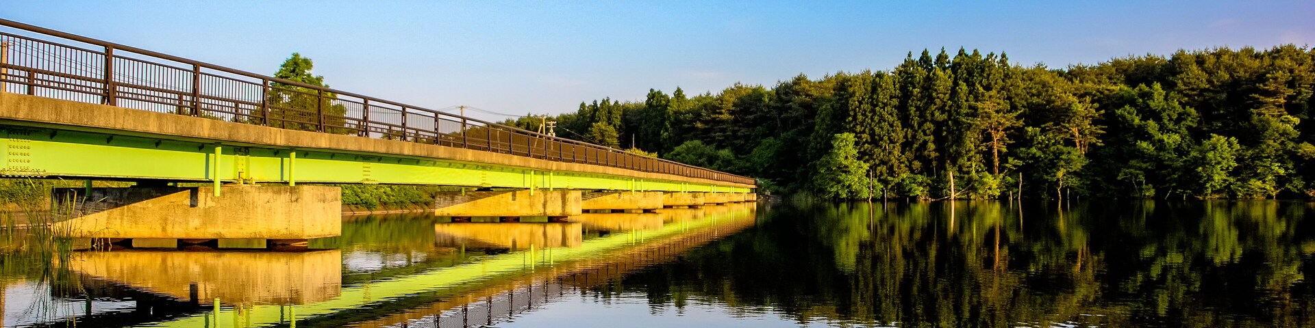 Uma ponte sobre águas calmas, com uma área arborizada ao fundo.
