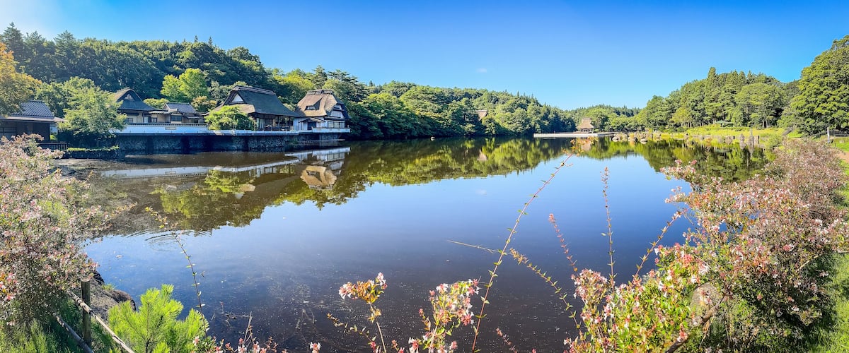 A serene lake with traditional Japanese architecture reflecting on the water, surrounded by lush greenery.