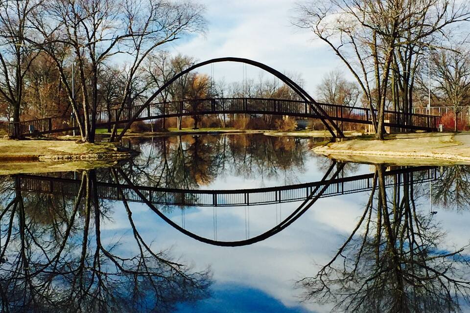 A metal bridge over a calm river with reflections of trees and sky.