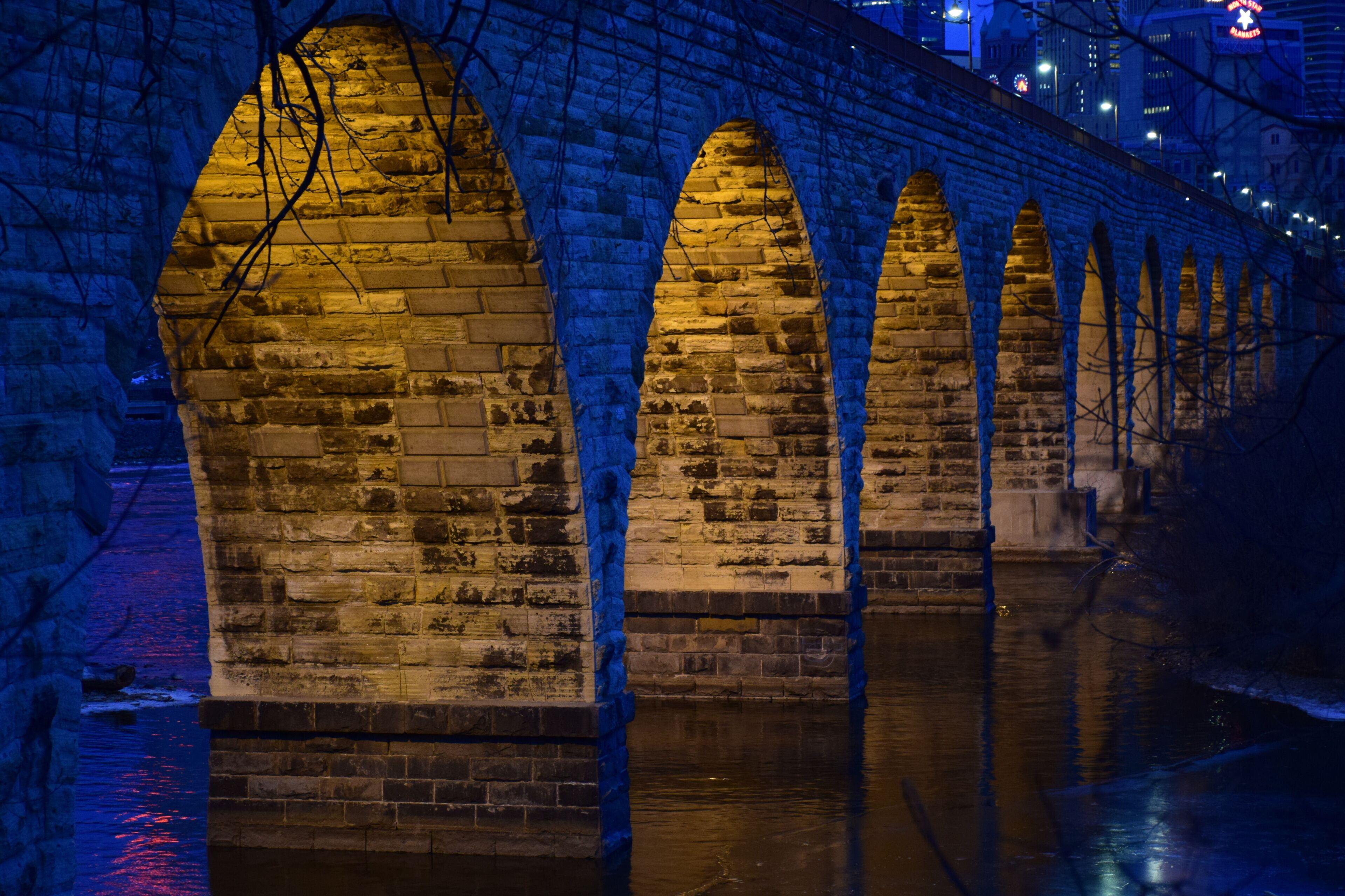 Uma ponte de pedra com várias arcos sobre a água, iluminada por iluminação artificial.