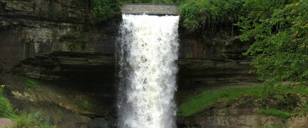 A waterfall cascading down a rocky cliff surrounded by greenery.