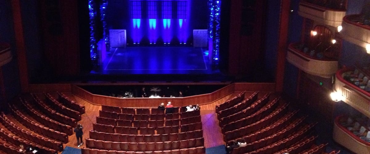 An indoor theater with a stage, rows of seats, and a balcony.