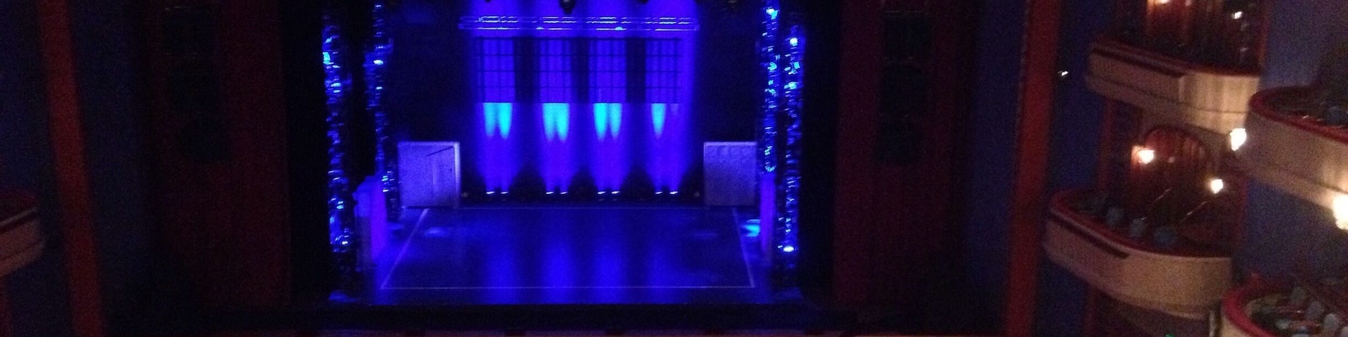 An indoor theater with a stage, rows of seats, and a balcony.