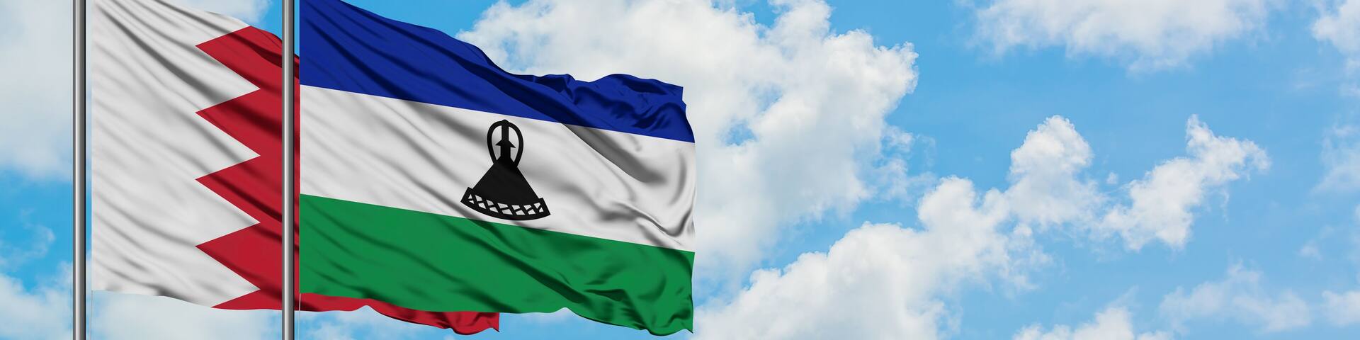 Bahrain and Lesotho flag waving in the wind against white cloudy blue sky together. Diplomacy concept, international relations.