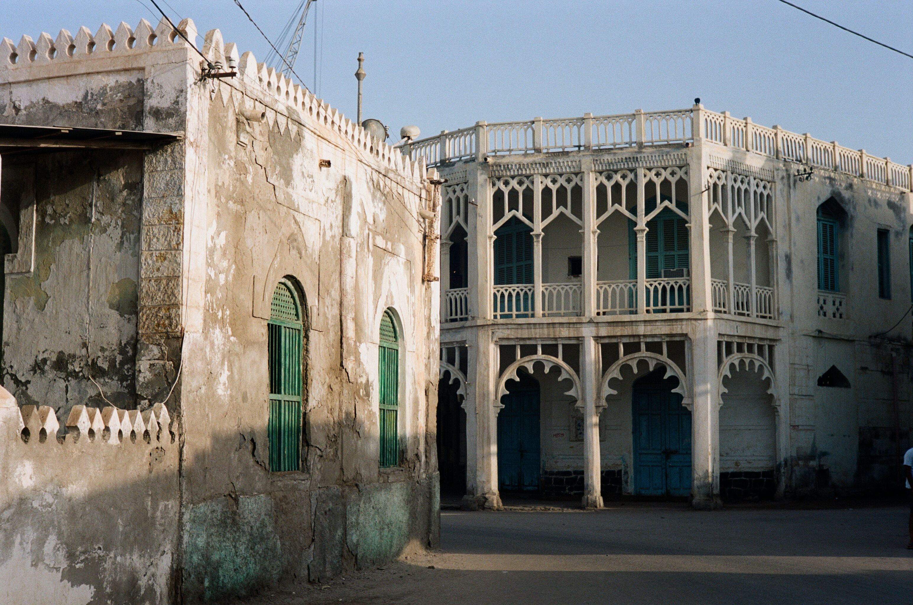 Um edifício histórico com portas em arco e persianas verdes, apresentando intrincadas varandas brancas e fachada desgastada pelo tempo.