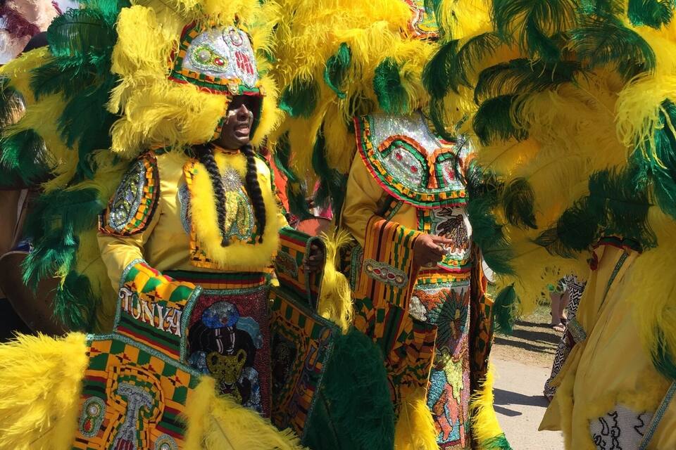 Performers in elaborate yellow and green costumes with feathered headdresses.