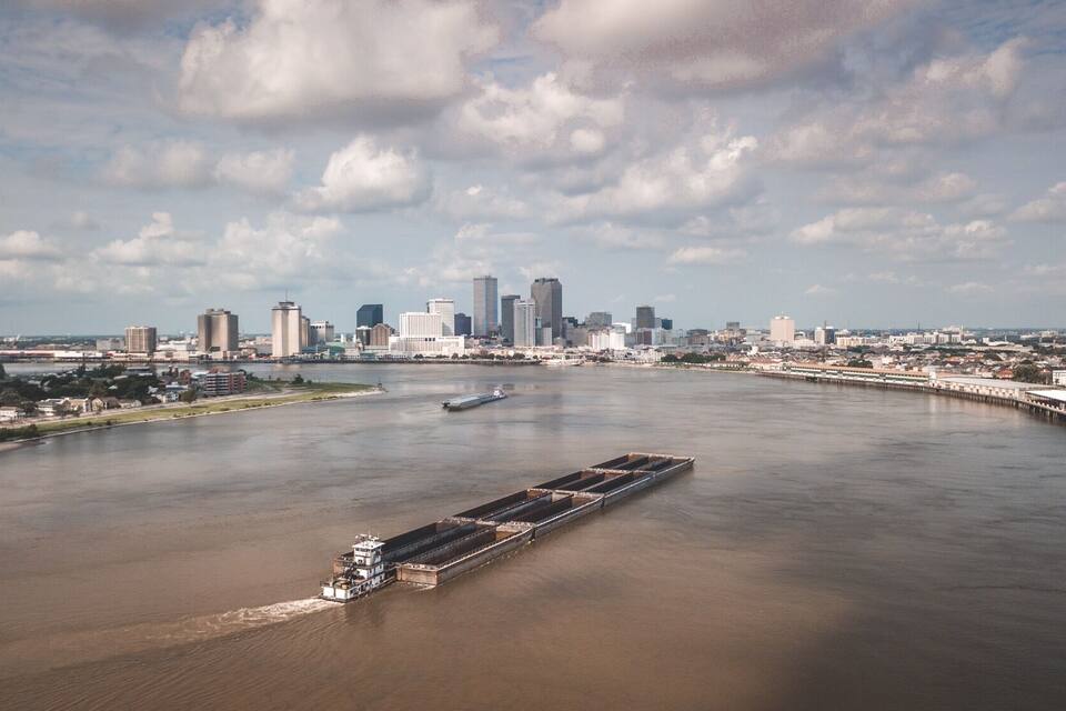 A river with a barge, a city skyline, and a bridge in the background.