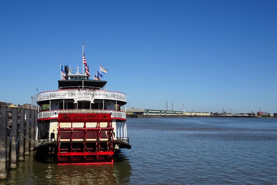 A steamboat docked at a pier with a clear blue sky and calm water.
